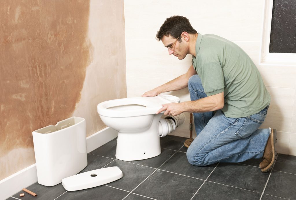 Plumber installing new toilet in bathroom.